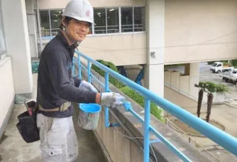 写真：白いヘルメットを被った作業員が学校2階の手すりに塗料を塗っている様子。